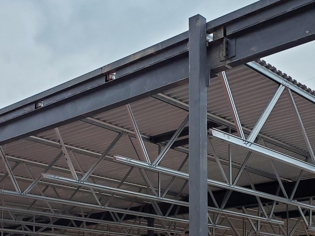 The photo depicts the roof of a metal structure with several support beams of various sizes throughout. 