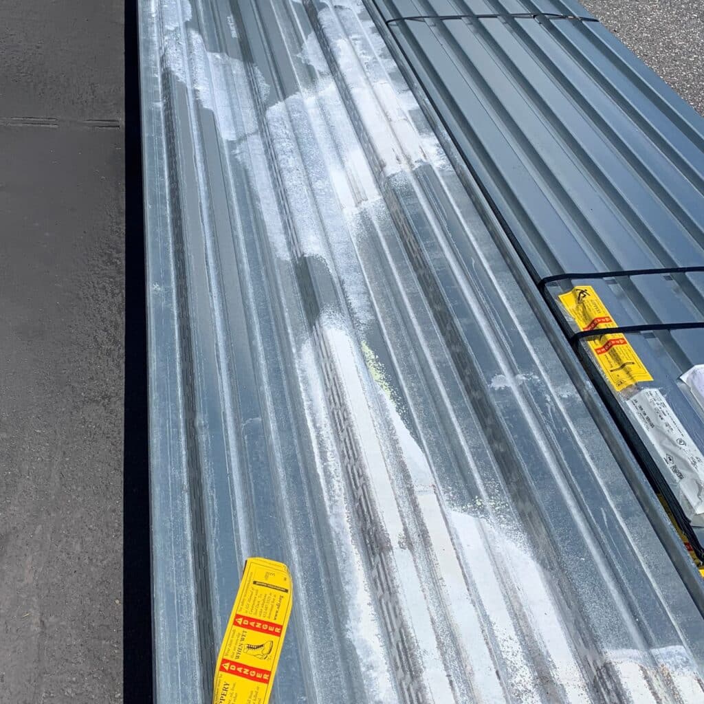 A large, metal roof decking pallet laid on pavement. The pallet is shiny silver with yellow stickers on it. 
